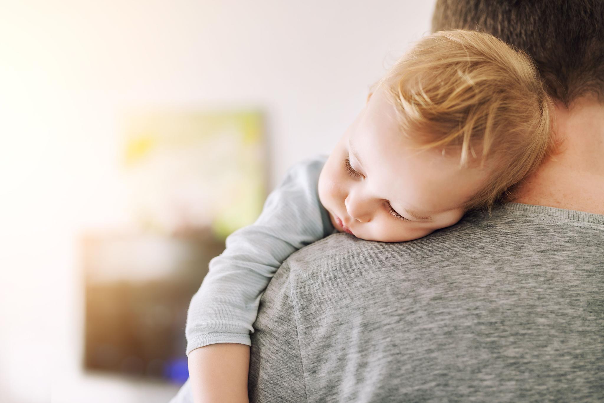 A tired baby sleeps on their father