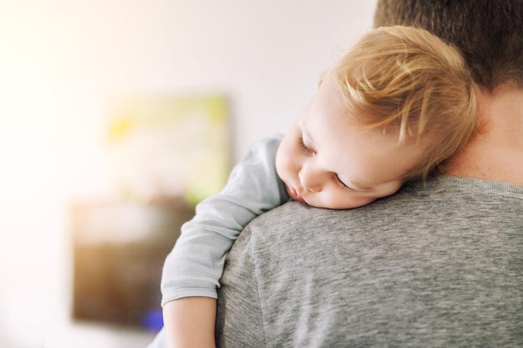 A tired baby sleeps on their father