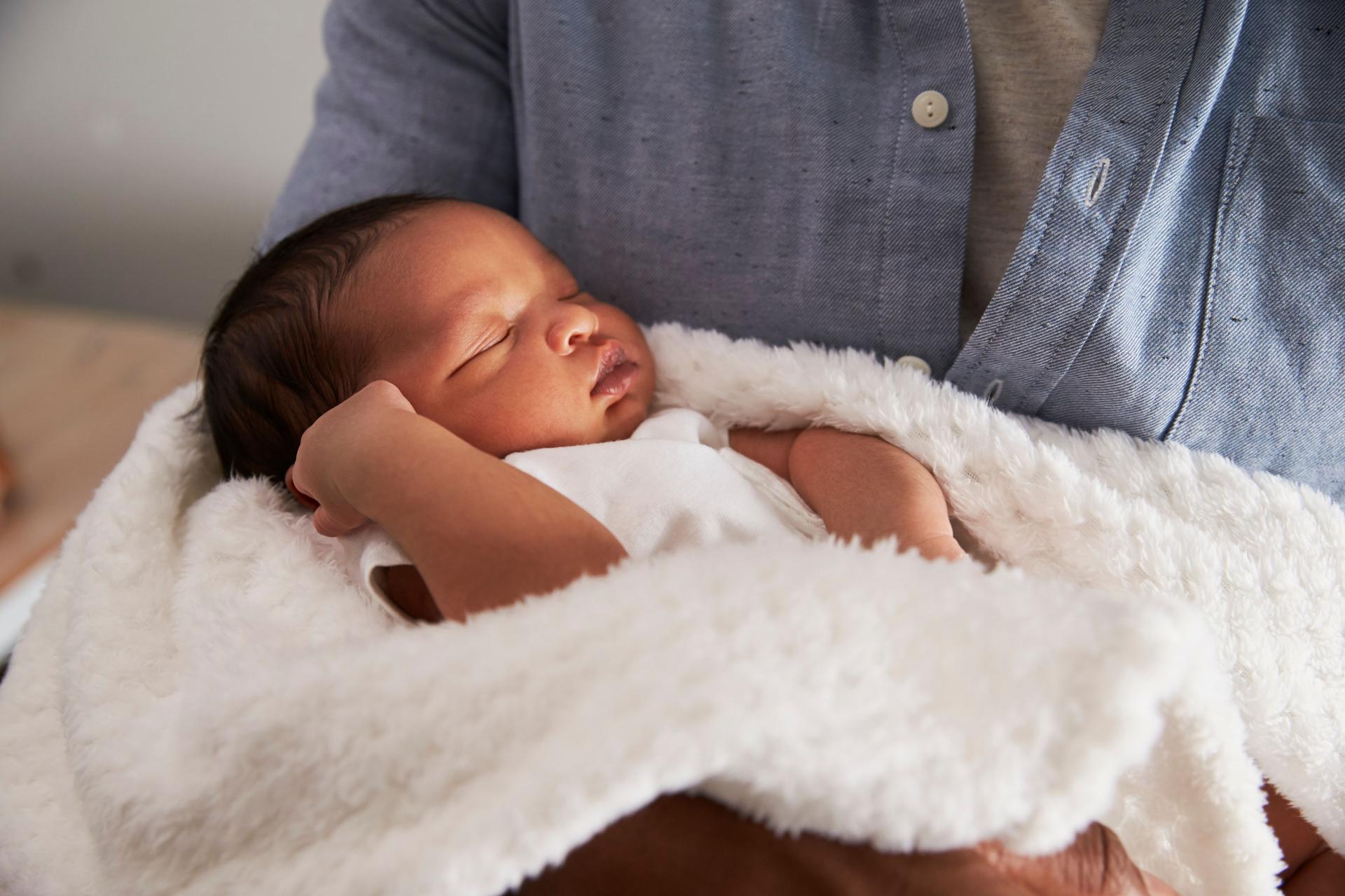 A baby sleeping in their parent's arms, looking sleepy and adorable.